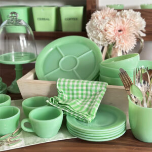 A collection of Fire-King Jade-ite plates, cups, bowls, with Jeannette Jadite canisters in the background.