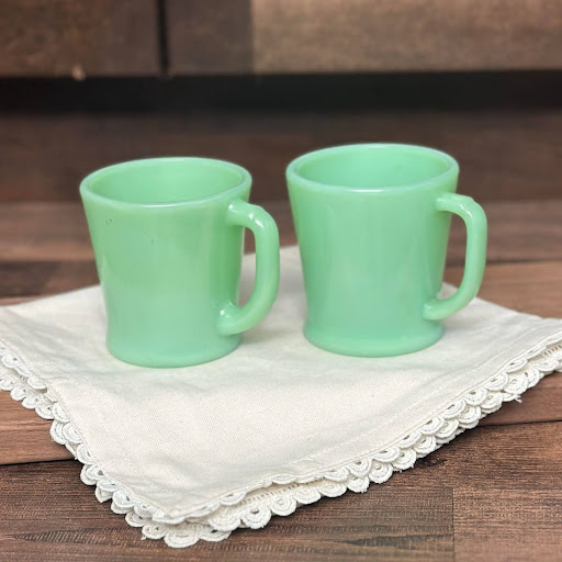 A group of six vintage Fire-King Jadeite D-handle mugs arranged on a wooden surface. Though they appear identical, slight differences in base design can affect their value.
