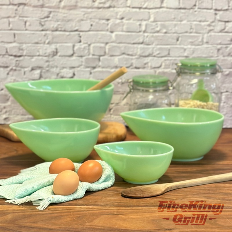 Styled photo of a Jadeite Swedish Modern mixing bowl set on a wood surface with eggs, a tea towel, and wooden spoon